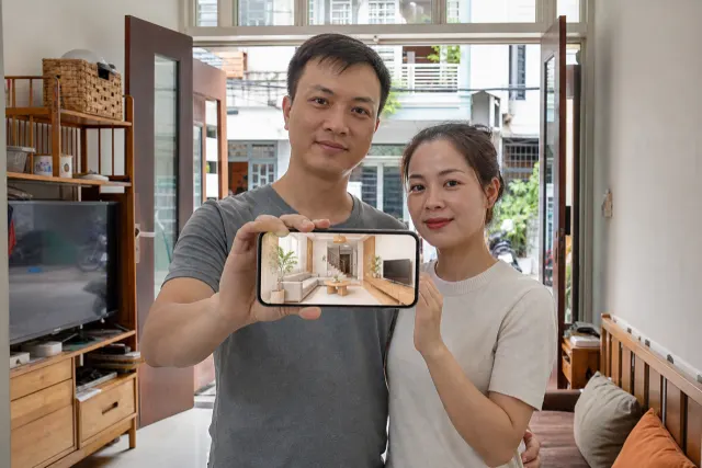 Hai người xem điện thoại hiển thị phối cảnh nhà do AI thiết kế, trong phòng khách có sofa be, gỗ sáng và ánh cửa sổ