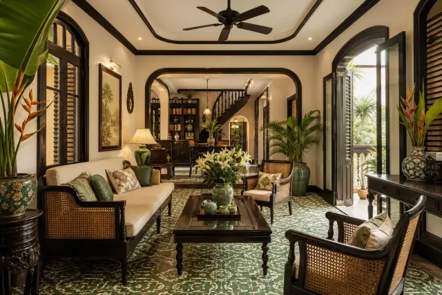 Phòng khách Indochine với sofa khung gỗ đan mây, sàn gạch bông họa tiết xanh, cửa vòm gỗ tối màu và quạt trần cổ điển