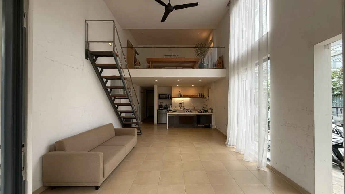 Nhà phố nhìn từ cửa trước, gác gỗ nửa sau trên bếp, thang sắt sát tường trái, sofa và cửa sổ cao phía trước vẫn thông tầng