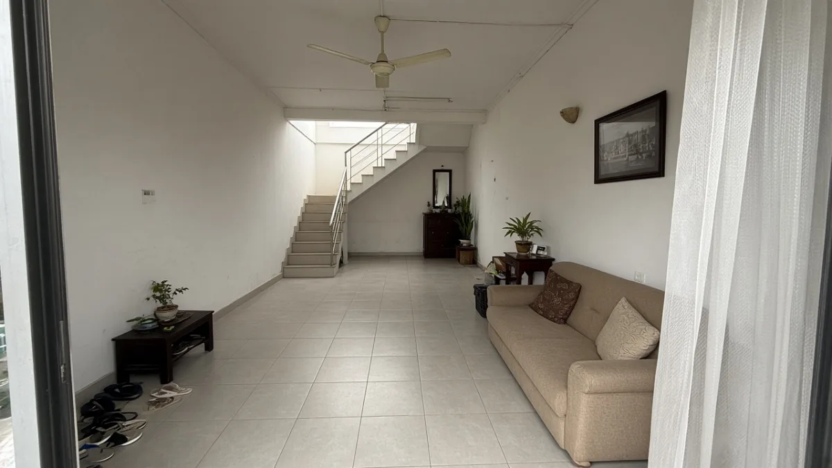 Nhà ống nhìn từ cửa trước, sofa dọc tường phải, cầu thang bê tông sát tường trái và ô sáng phía trên thang